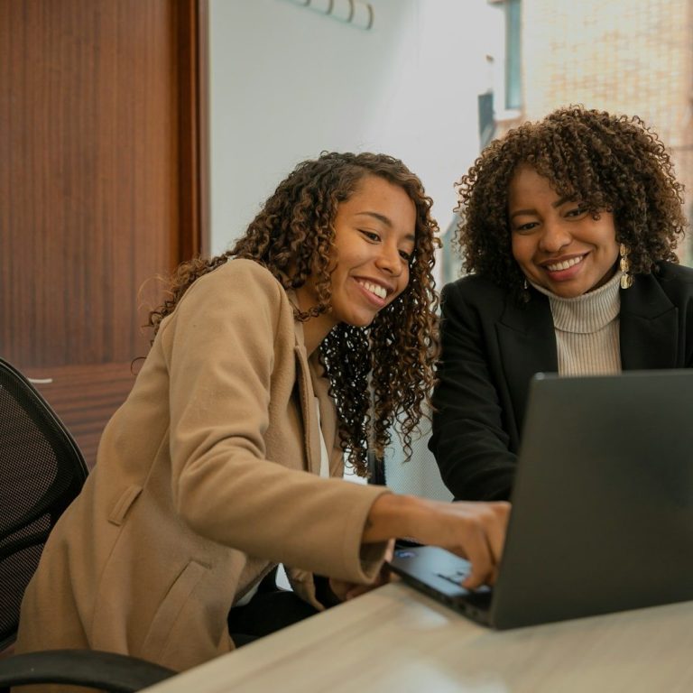 Deux femmes souriantes collaborent sur un ordinateur portable dans un bureau. Deux femmes souriantes collaborent sur un ordinateur portable dans un bureau.