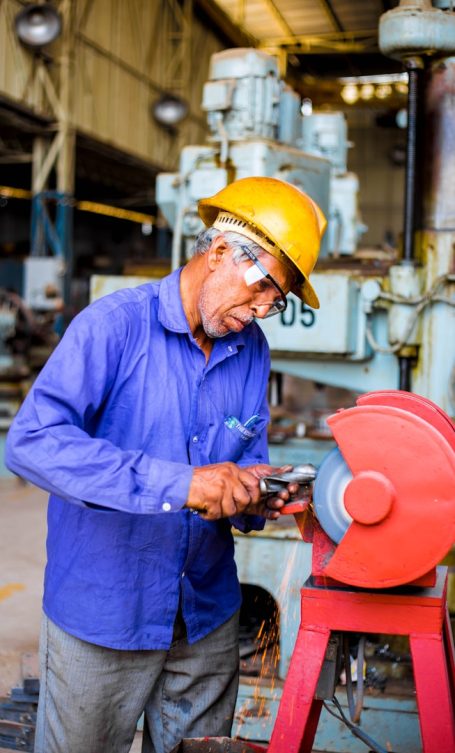 Homme en vêtement de travail Homme en vêtement de travail utilisant une meule à l'intérieur d'un atelier.